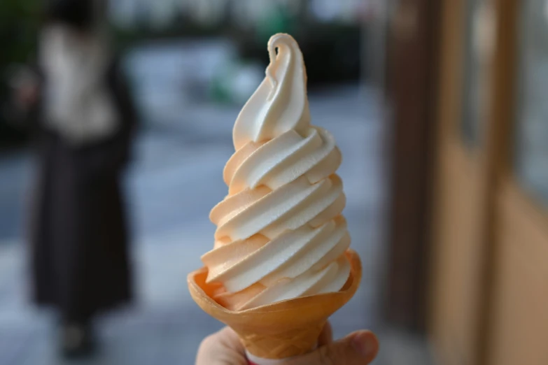 a person holding up an ice cream cone with white frosting