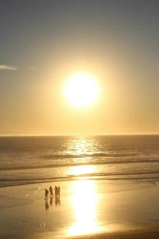 three people walking along the beach at sunset