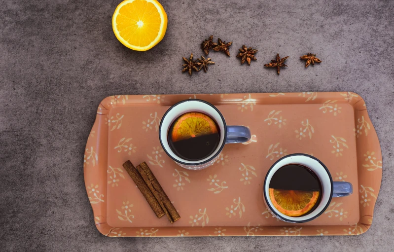 two cups of coffee on a tray beside an orange