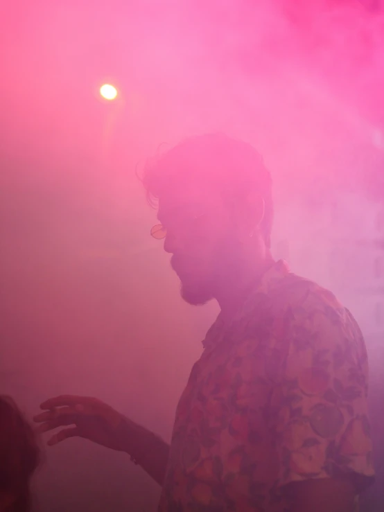 man in a yellow shirt standing under some pink smoke