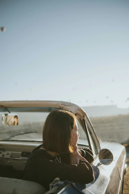 a woman with long hair sits in the drivers seat of a car