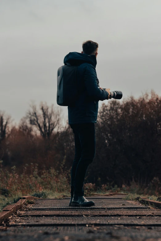 man in jacket holding camera on side of walking path