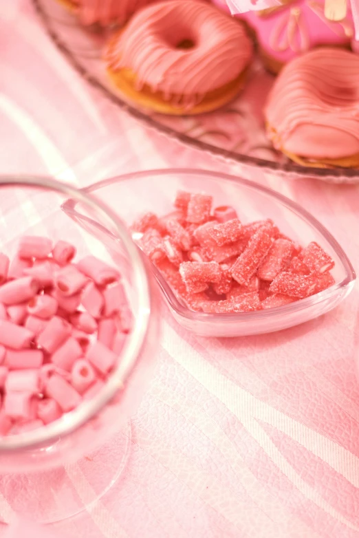 pink frosted doughnuts in glass plates and bowls next to candy