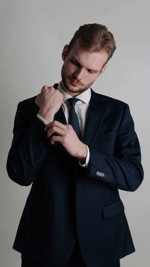 a young man adjusting his tie while standing in front of a grey background