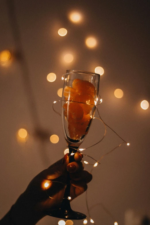 a person holds a wine glass in front of sparkling lights