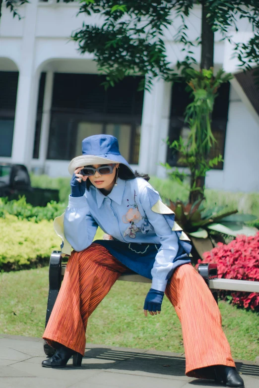 a young woman with a long skirt and hat sits on a park bench