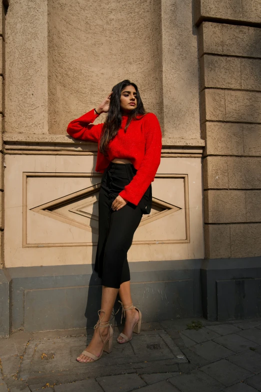 a woman wearing a red sweater leaning against the side of a building