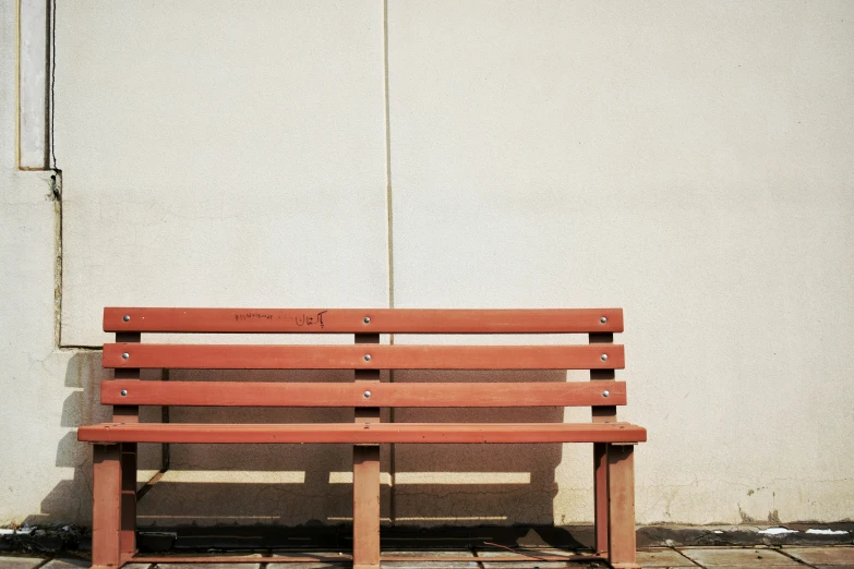 a lone wooden bench sitting in front of a white wall