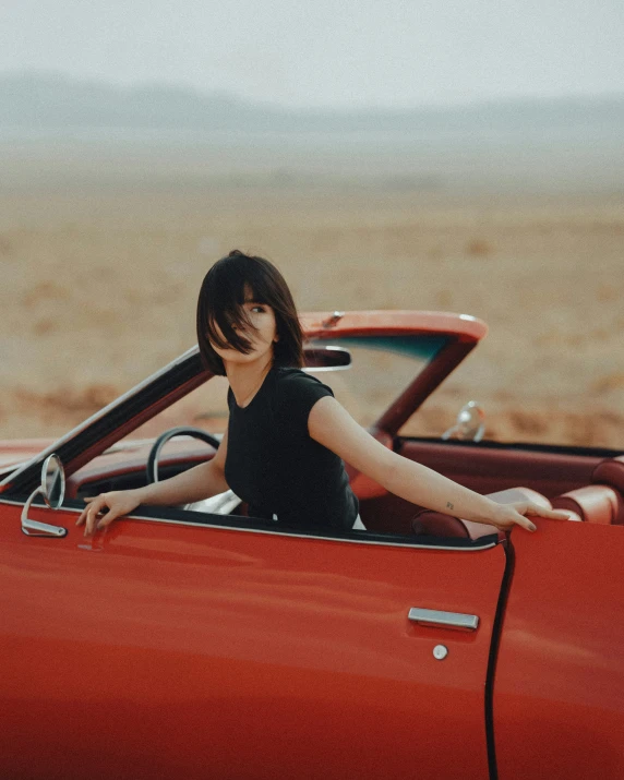 a woman leaning on the dashboard of a red vintage car