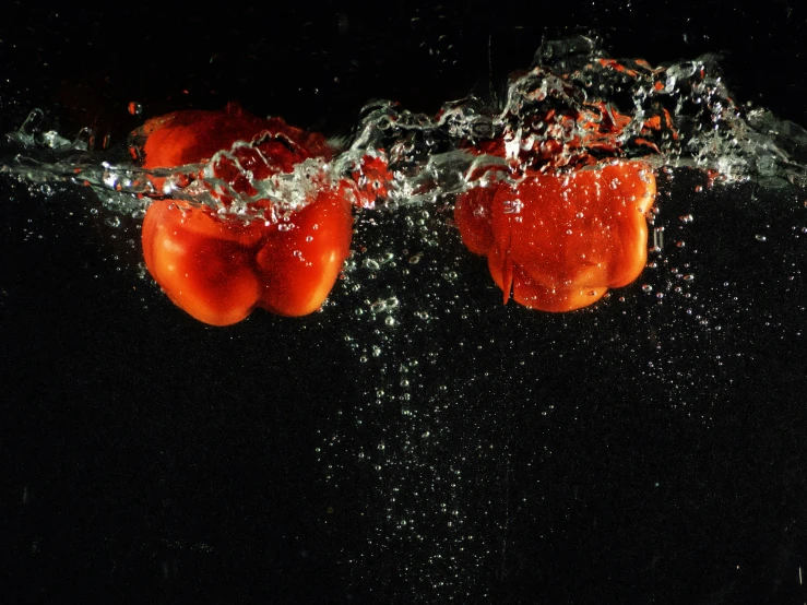 three tomatoes floating through water with their tops dropped