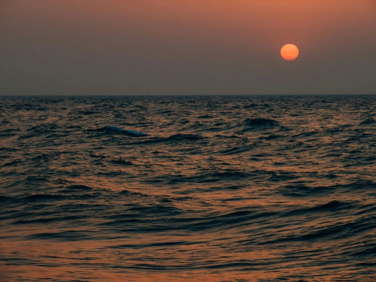 the sun sets over an ocean wave in front of a boat