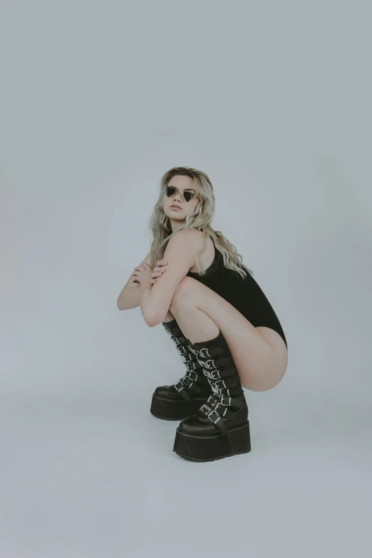 a woman sitting down wearing a short black outfit and a pair of boots