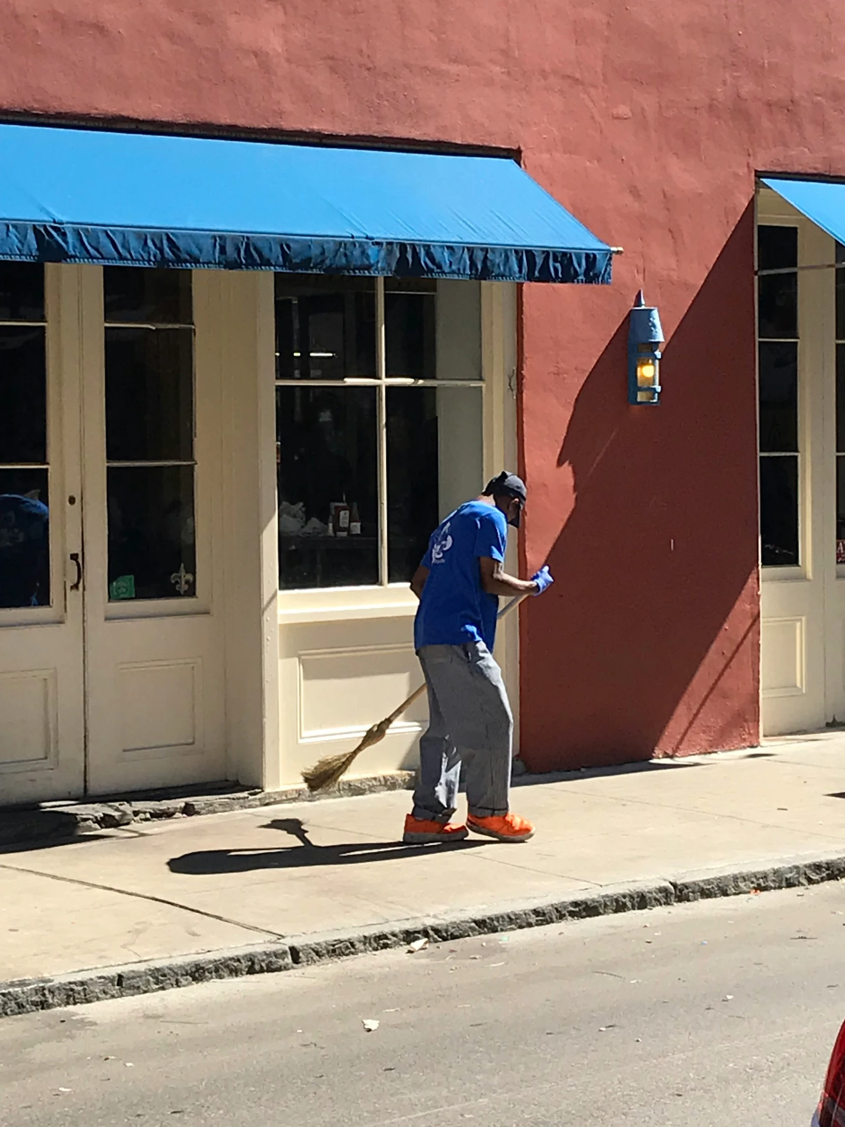 man sweeping sidewalk next to a storefront with blue canopy