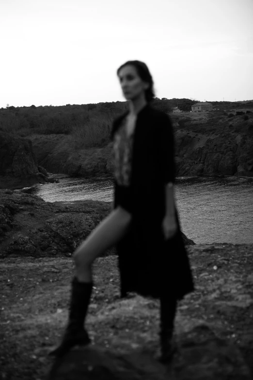 a black and white image of a woman in a dress standing by a lake