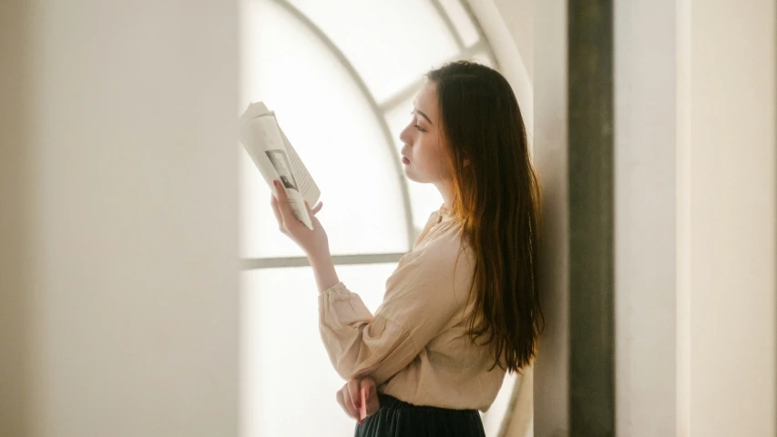 a young woman looking out the window while reading a book