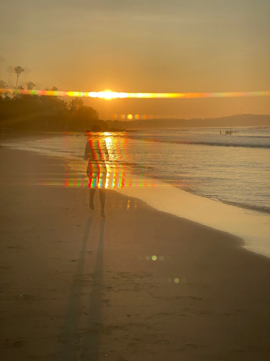 the person is walking along the beach while the sun goes down