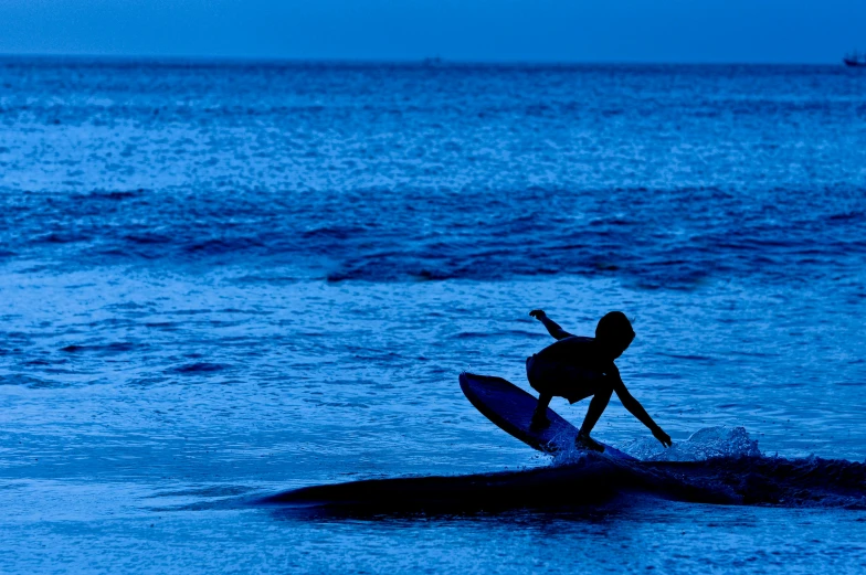 a silhouetted person standing on a surfboard in the ocean