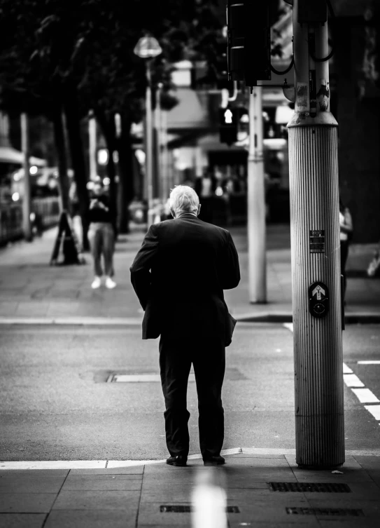 a black and white image of an elderly man leaning against a traffic light