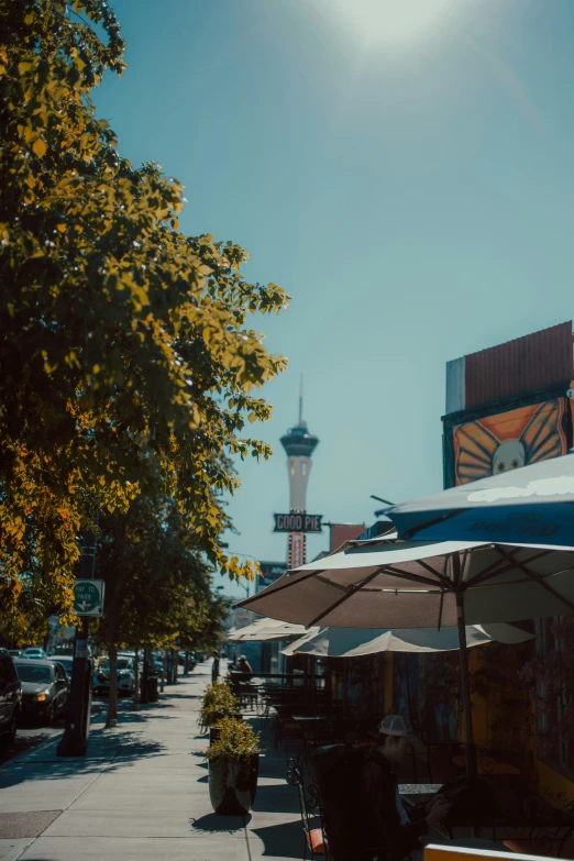 a side street covered in umbrellas and tables under a tall white tower