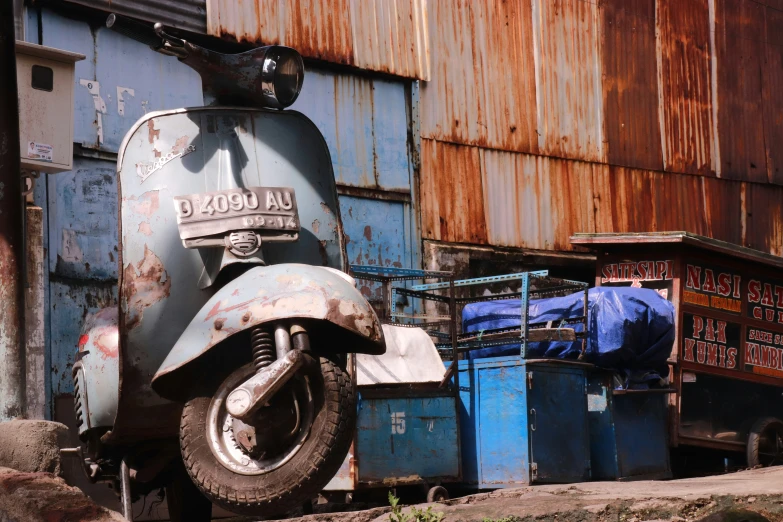 a moped with the word daunt on it in front of a rusty wall and dumpster