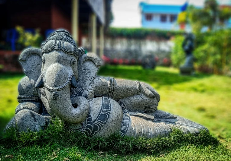an elephant made of cement sitting on top of some grass