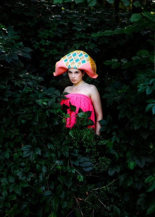 a woman in a hat is standing among some bushes