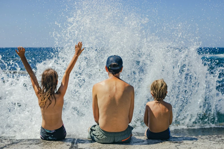 three people sitting on the rocks at the beach