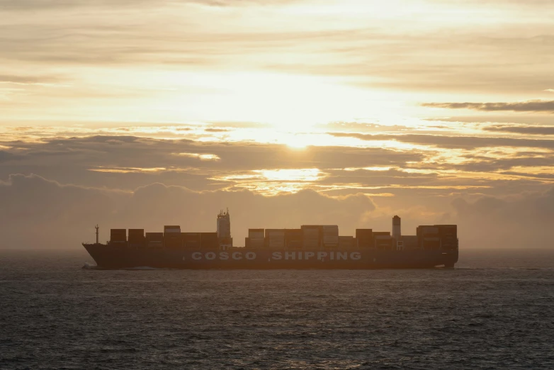 the sun sets behind the container ship at sea