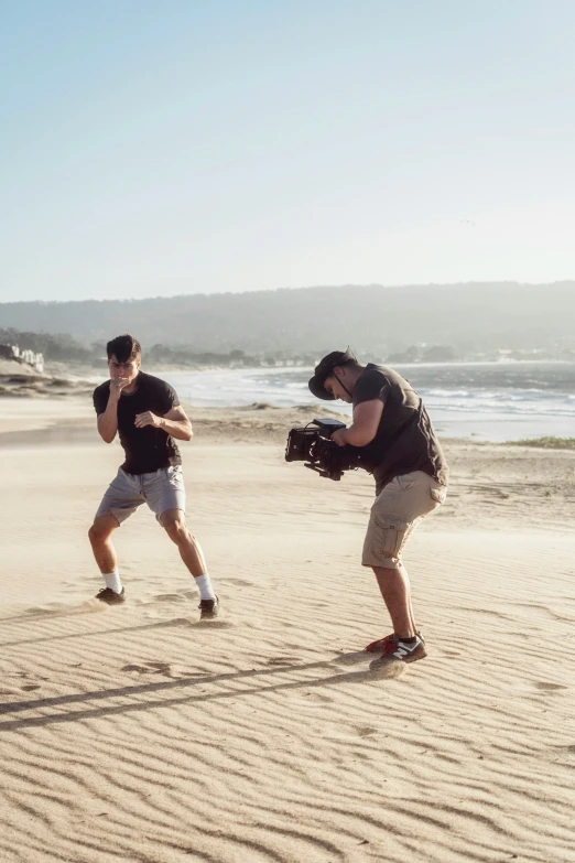 two guys standing in the sand with a camera