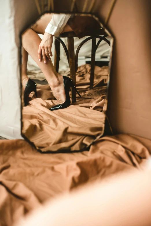 woman in heels and shirt on a bed looking at herself through a mirror