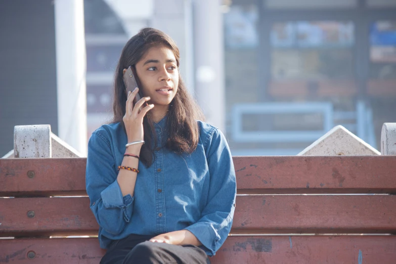 a woman sitting on a wooden bench talking on a cell phone