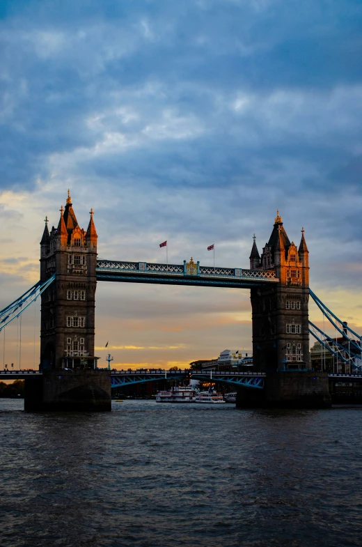 a tower bridge with boats passing over it at sunset