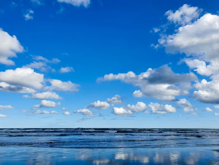 a single bench is next to the ocean under blue skies