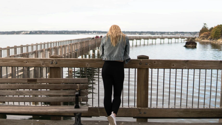 there is a girl standing on the bench looking at the water