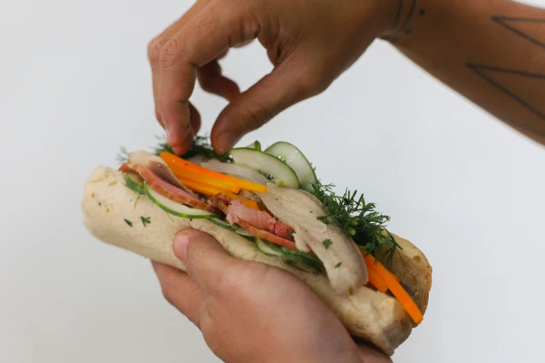 hands holding up a sandwich with lettuce, tomatoes, and cucumbers