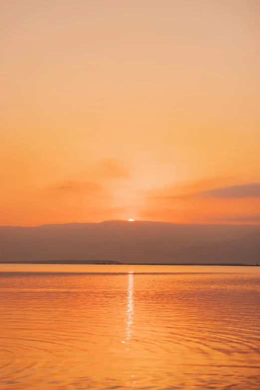 the sun setting over the water with a boat at the beach