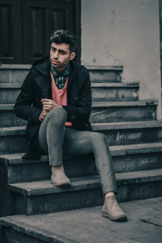 a man is sitting down wearing a jacket and patterned pants