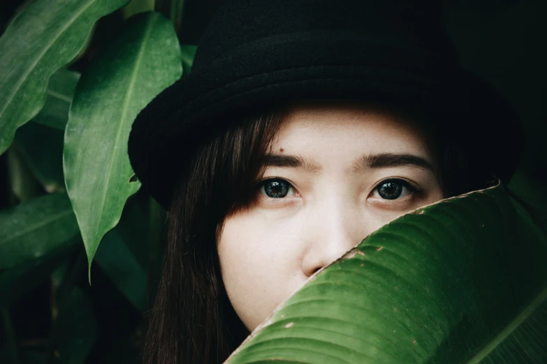 a woman with a hat looking out from behind some leaves