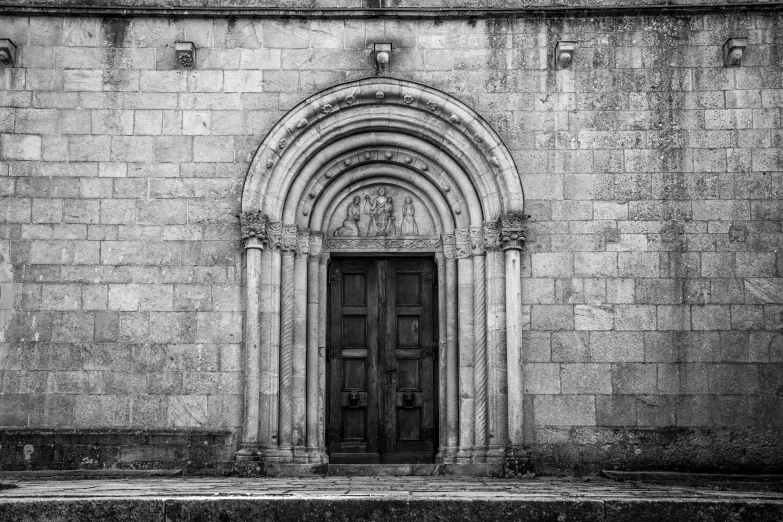 a stone building with a double door and two people walking on a street