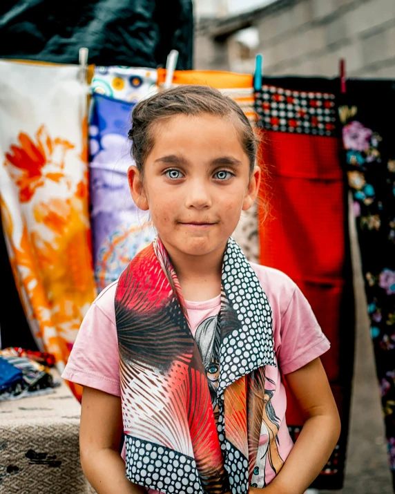a small girl stands in front of a bunch of clothing