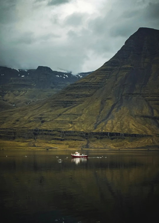 a small boat on the calm water with mountains in the background