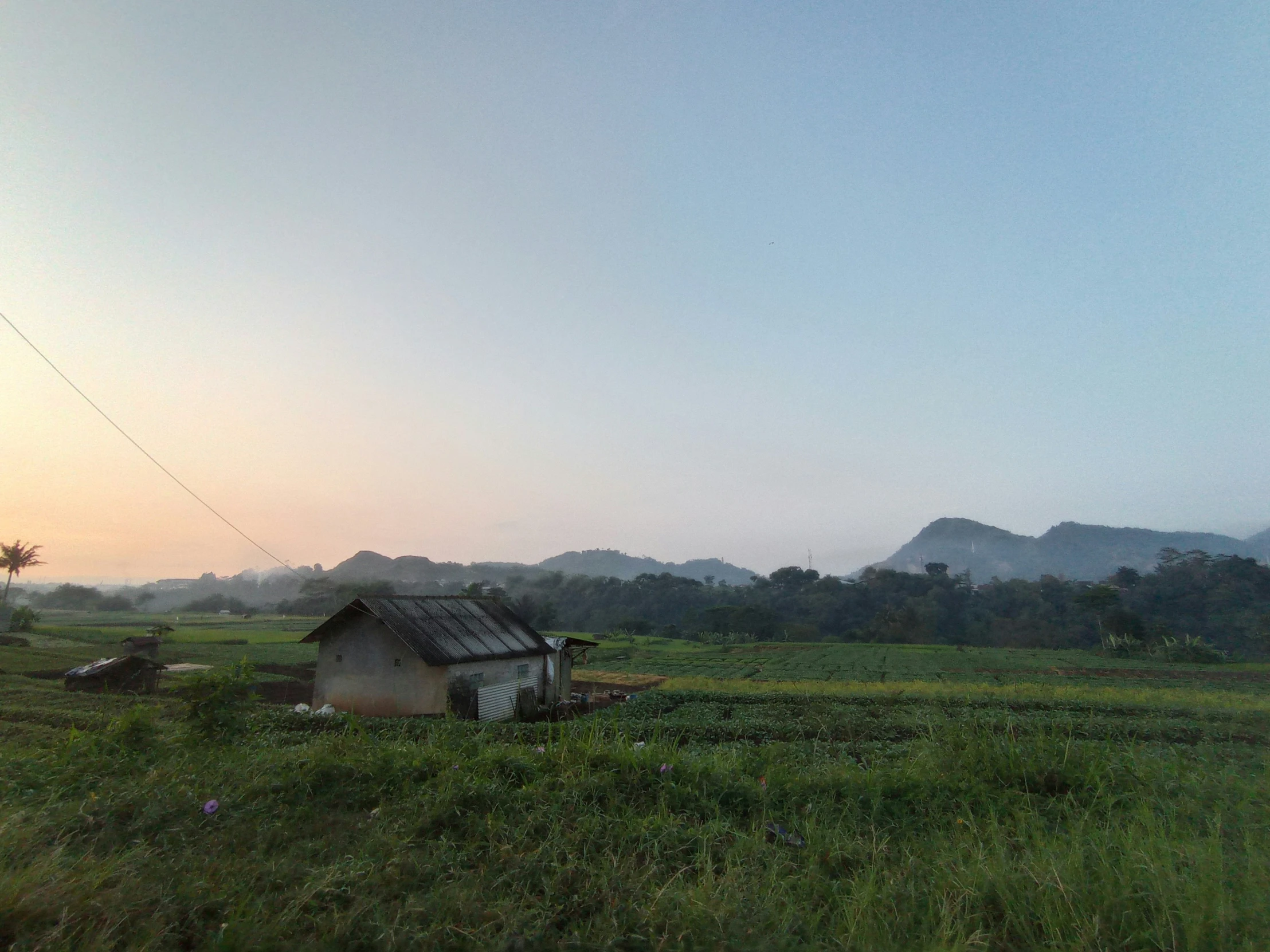 a house sitting in the middle of the grass with mountains in the background