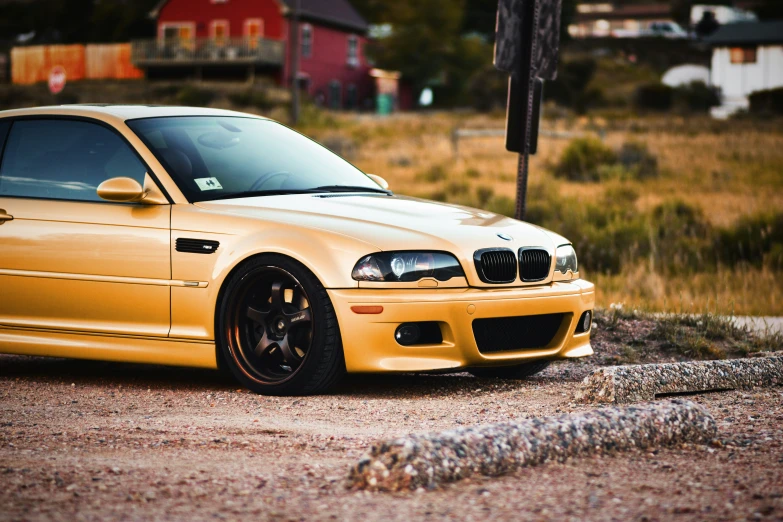 a gold bmw parked in front of a red barn