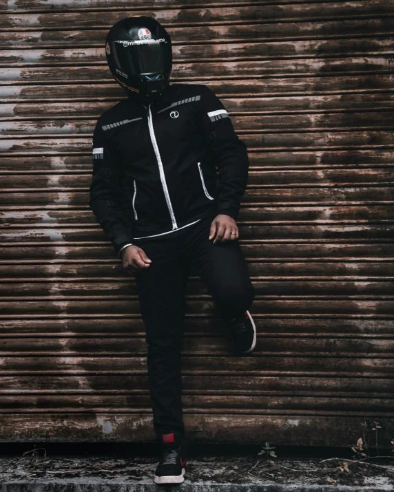 a man wearing a helmet standing against a rusted garage door