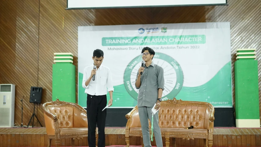 two men speaking at a seminar in front of a green stage