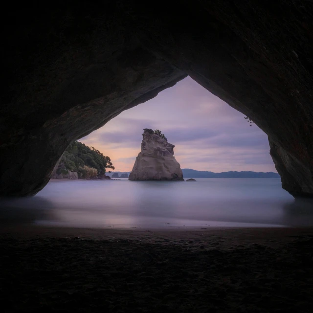 a beach near the ocean with rock formations on the far shore