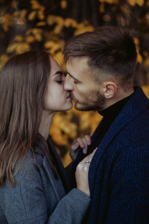 a couple emcing each other as they stand close to the ground in front of yellow leaves