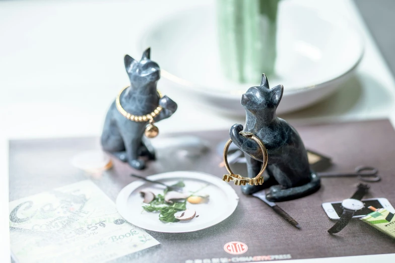 two figurines on a plate sit beside a vase and place setting