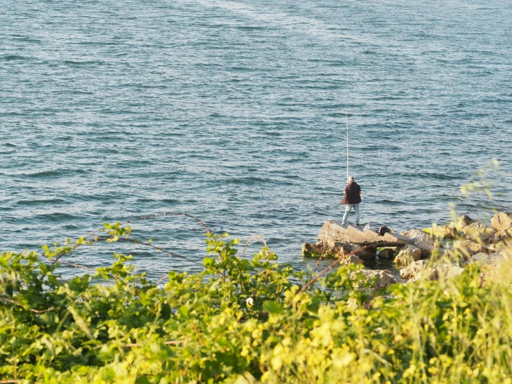 a man standing on rocks near the ocean fishing