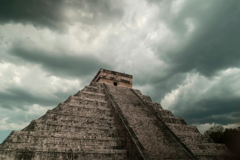 a very tall pyramid sitting under clouds and some dark colored sky